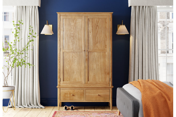 Beige wooden armoire in blue bedroom with gray curtains and gray bed with orange throw