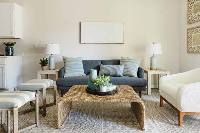 Living room with blue sofa, woven coffee table, and striped pillows.