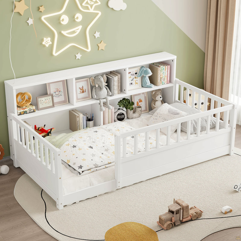 Un lit de plancher en bois de taille simple avec une barrière de sécurité de style clôture, une fonction décorative de rangement latérale et la couleur est blanche