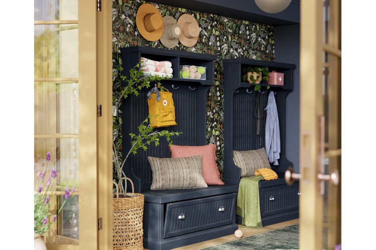 Two blue hall trees filled with throw cushions next to one another in an entryway. Black floral wallpaper and a woven planter with a small tree inside