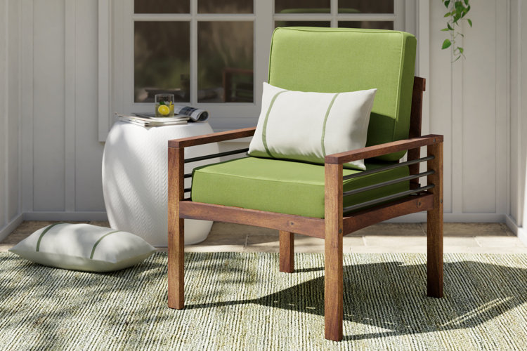 teak outdoor chair with a bright green cushion, striped outdoor pillow, and a white garden stool
