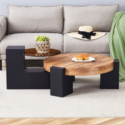 Table basse ronde moderne simple à double couche - Plateau en verre brun transparent avec pieds en panneau de fibres à densité moyenne noirs en forme de L. La conception détachable peut rendre l'utilisation de l'espace plus flexible.