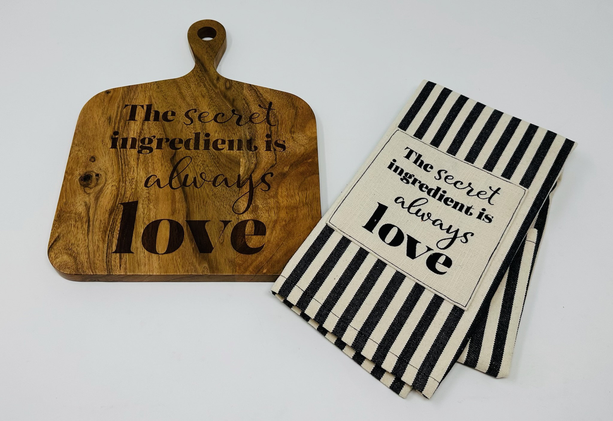 https://assets.wfcdn.com/im/49326927/compr-r85/2551/255146044/square-cutting-board-with-black-striped-tea-towel-with-the-words-secret-ingredient-is-always-love.jpg