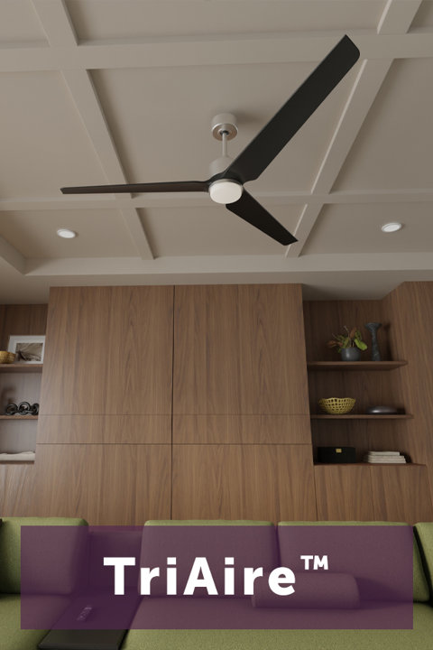 Modern TriAire ceiling fan with dark blades and integrated light fixture in a contemporary living room with wood paneling.