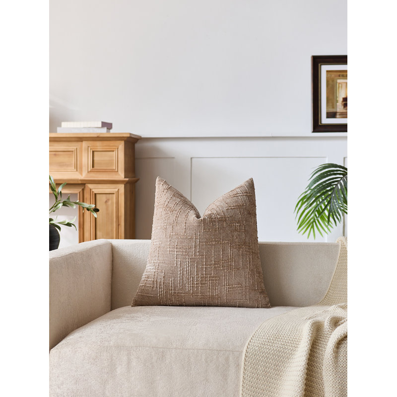 Square throw pillow in tan textured chenille fabric on a sofa