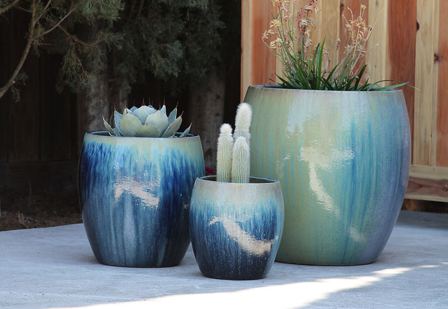Three rounded, glazed ceramic planters in varying sizes and shades of blue and green, each holding a different succulent or ornamental plant on a concrete patio.