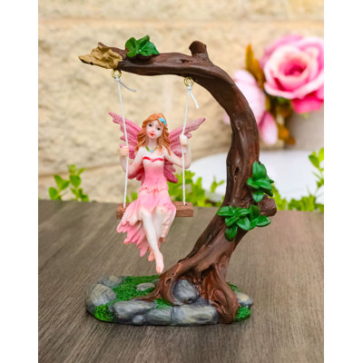 Figurine de fée tribale rose sur une balançoire à une branche d'arbre avec des ailes roses et des cheveux ambrés