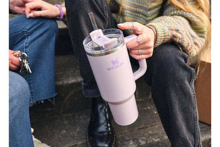 pink stanley tumbler with straw in the hands of a woman wearing rings sitting next to a man holding keys