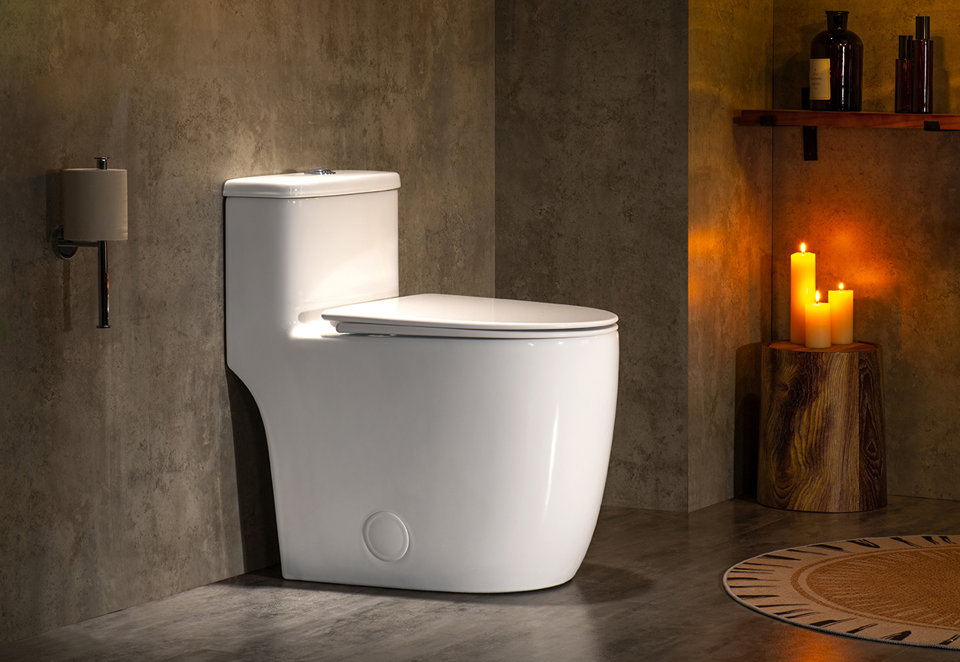 White one-piece toilet with a sleek, modern design in a dimly lit bathroom with concrete-style walls, candles, and natural wood accents.