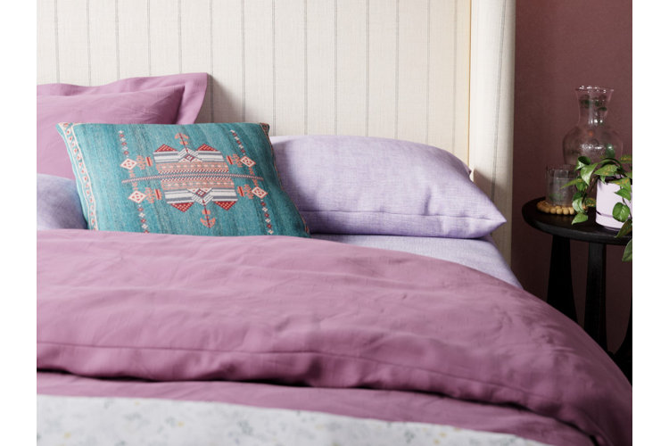 Purple bedroom idea, featuring a light purple comforter, purple sheets, and a blue throw pillow on a white upholstered bed.