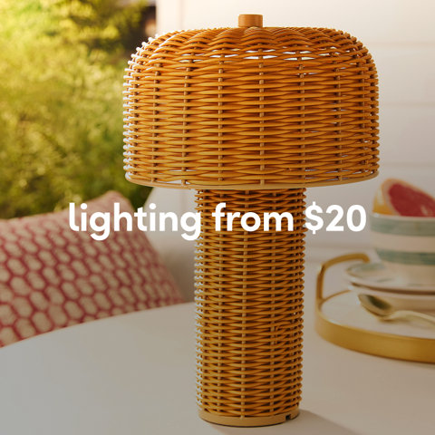 A mushroom-shaped outdoor table lamp made of natural tan wicker on a white patio table from $20.