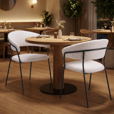 Ensemble de deux chaises de salle à manger avec accoudoirs, dossier partiellement ouvert, en fausse fourrure crème et noire, bois et acier.