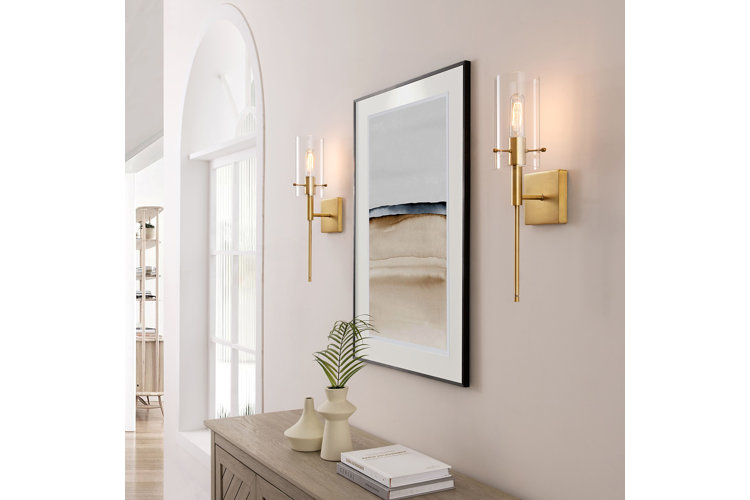 Hallway with a pair of gold wallchiere wall sconces on either side of an abstract painting and above a wood accent cabinet.