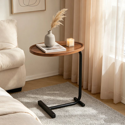 Table d'appoint brune en forme de C, placée à côté du canapé du salon, simple et pratique sans prendre de place