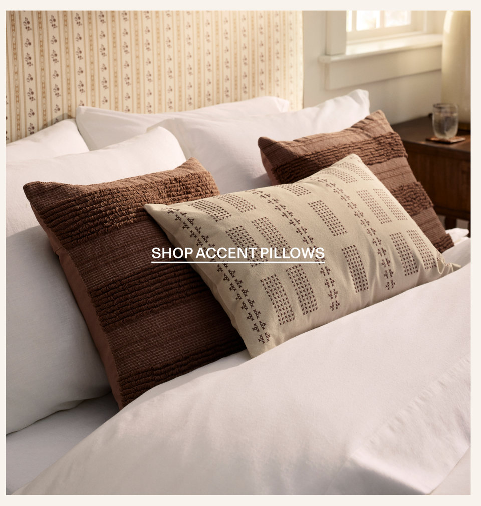 Textured brown and patterned accent pillows on a white bed with the text Shop Accent Pillows.