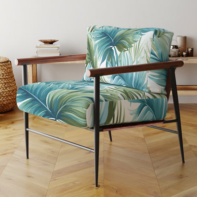 Fauteuil côtier en velours à motif tropical bleu et vert, avec accoudoirs et coussins décoratifs à feuilles tropicales.