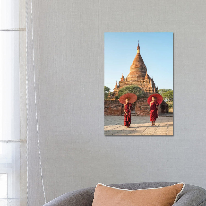 Two Young Novice Monks With Red Umbrellas Standing In Front Of A Temple, Bagan, Myanmar by Jan Becke - Wrapped Canvas Print