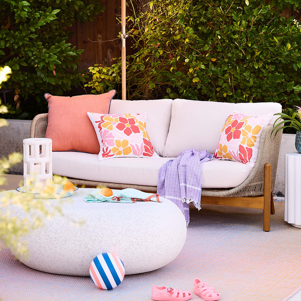 Terrasse extérieure avec un canapé blanc, des coussins, une table basse ronde en béton et des sandales d'enfant.