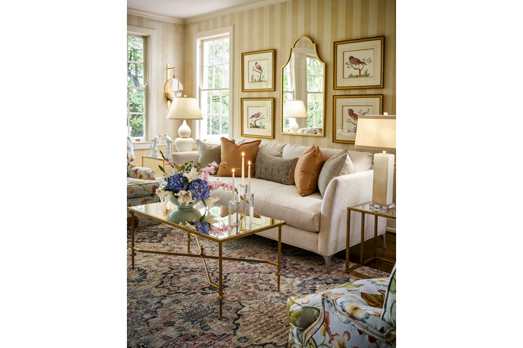 Gold living room color palette with gold striped wallpaper, gold picture frames, and a beige sofa.
