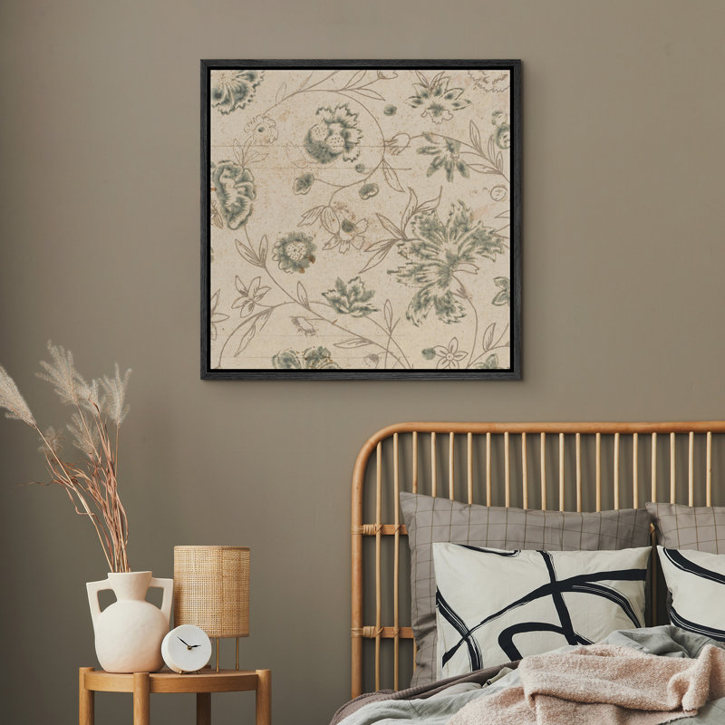 Square botanical wall art with a vintage green floral print in a black frame hanging above a rattan headboard.