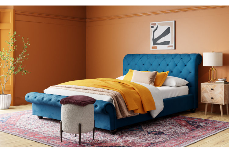 blue velvet bed with yellow bedding. white ottoman. yellow walls and red area rug