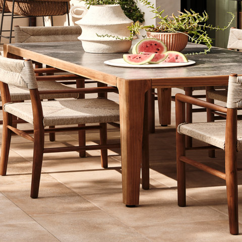 Outdoor dining table with watermelon slices, vase, and potted plant.
