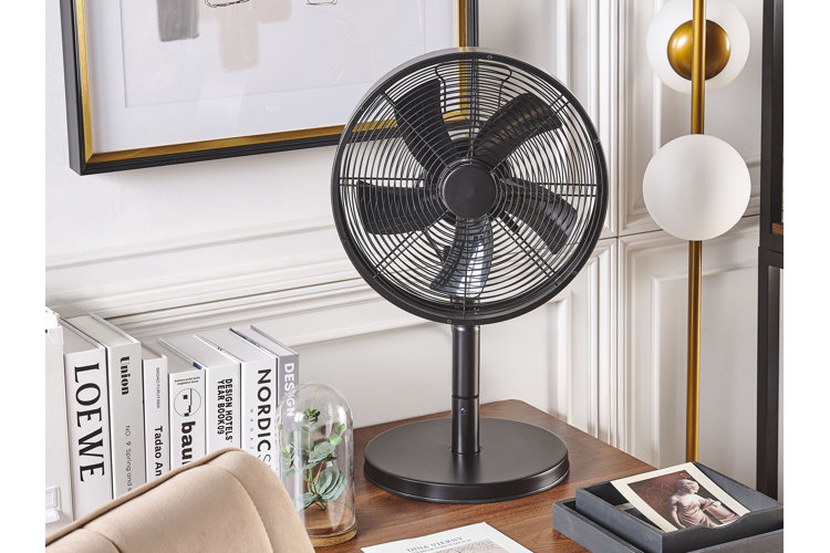 small black table fan sitting on a desk next to a stack of books