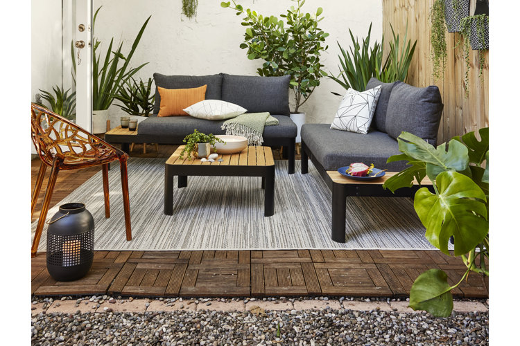 A small patio made of deck tiles with an outdoor seating area and green plants.