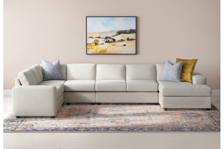 L-shaped ivory sectional and blue and orange Oriental rug under an abstract pastel landscape painting