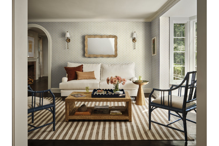 Cottage-style living room with a striped rug, a cream sofa, vintage wallpaper, and black wicker accent chairs.