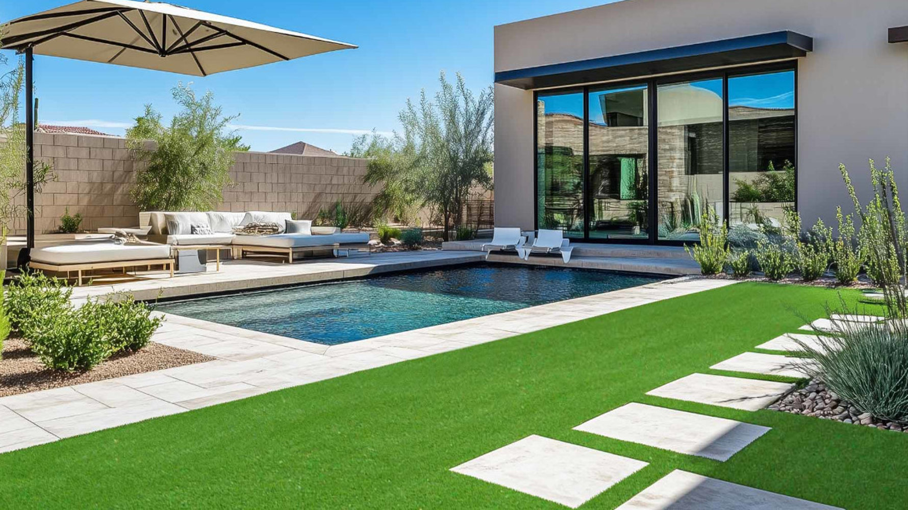 Patio arrière moderne comprenant une piscine, un coin salon avec un grand parasol et des dalles de pierre intégrées dans une pelouse verte à côté d'une maison contemporaine.