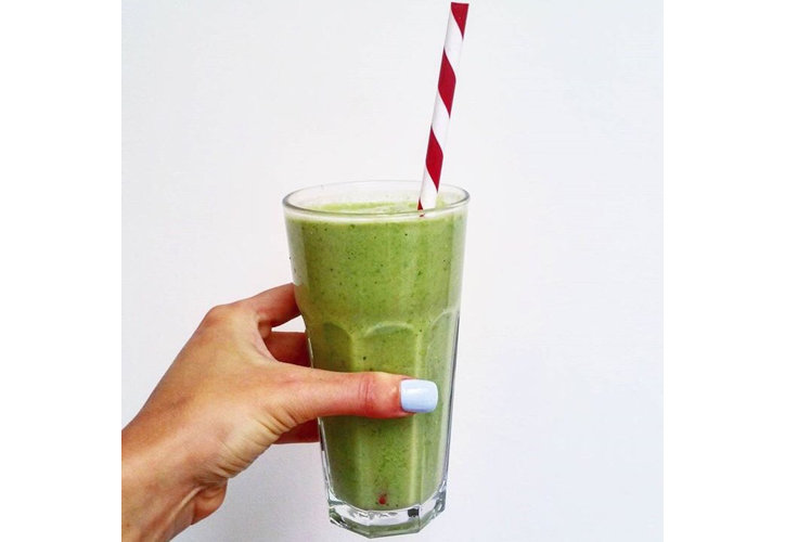 Woman's hand holding a tumbler glass of green breakfast smoothie with a red and white straw.