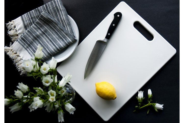 plastic cutting board with a lemon and a knife sitting on it, next to a vase of flowers and a kitchen towel