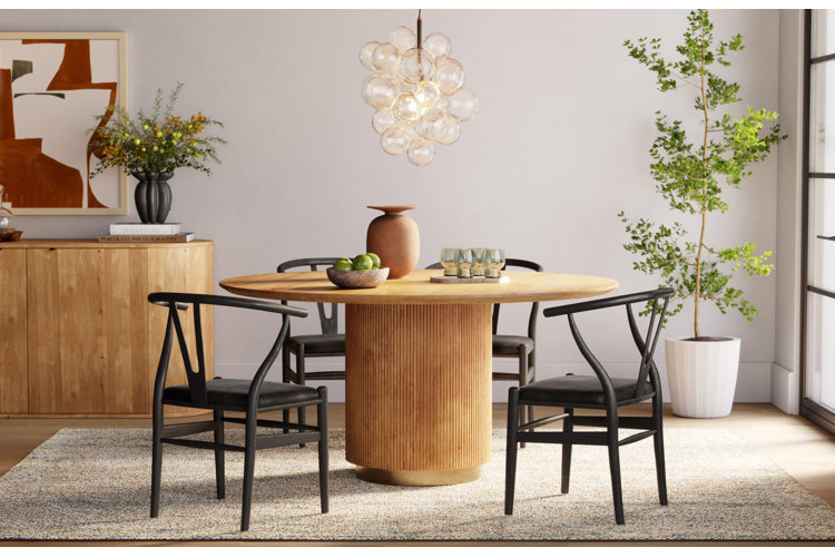 Dining room with a modern wood pedestal dining table, black wishbone dining chairs, a sputnik chandelier, and a faux tree.