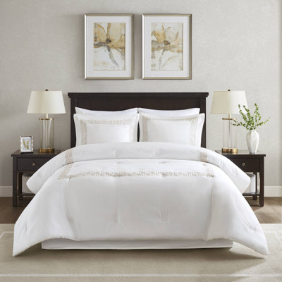 White comforter set with gold Greek fret embroidery border on a bed, including matching shams and a bed skirt.