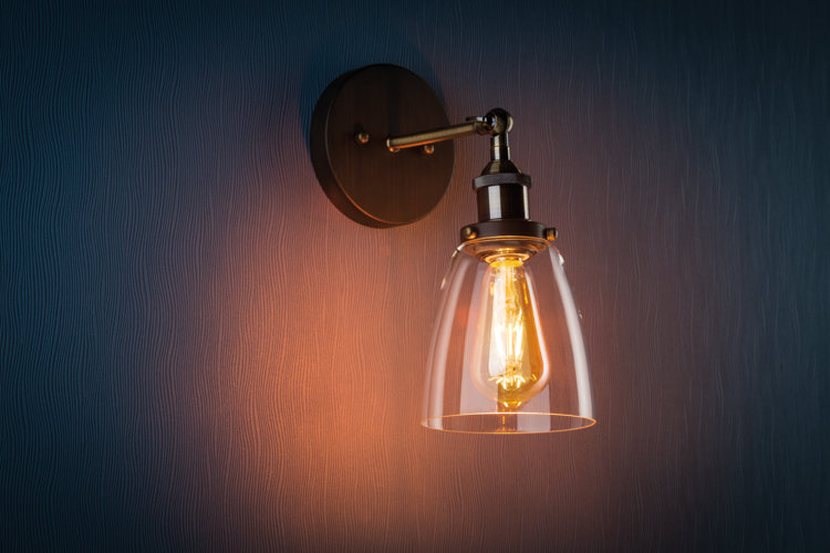 metal and glass wall sconce with a warm lightbulb