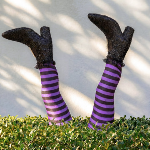 Piquet de jardin d'Halloween en forme de jambes de sorcière avec des bas rayés planté dans des arbustes