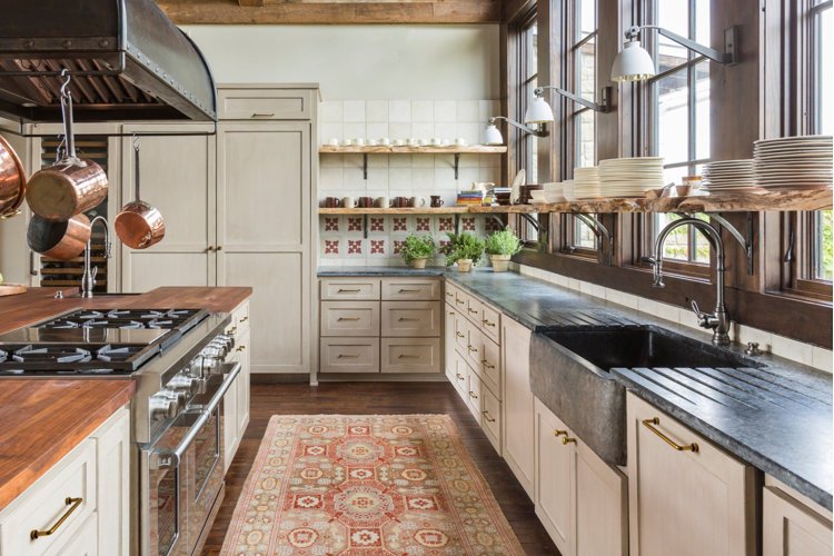 Rustic galley kitchen with a wood kitchen island and a built-in gas stove across from a set of granite countertops and a sink.