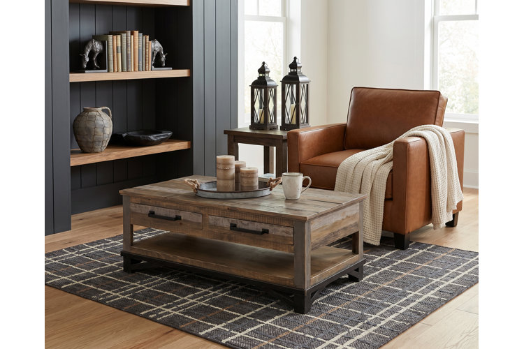 Industrial farmhouse-style living room with a leather armchair, distressed wood coffee table, plaid woven area rug, and galvanized metal decorative accents.