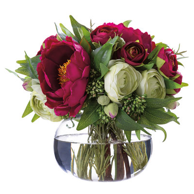 Composition florale artificielle de renoncules, pivoines et ruscus dans un vase en verre