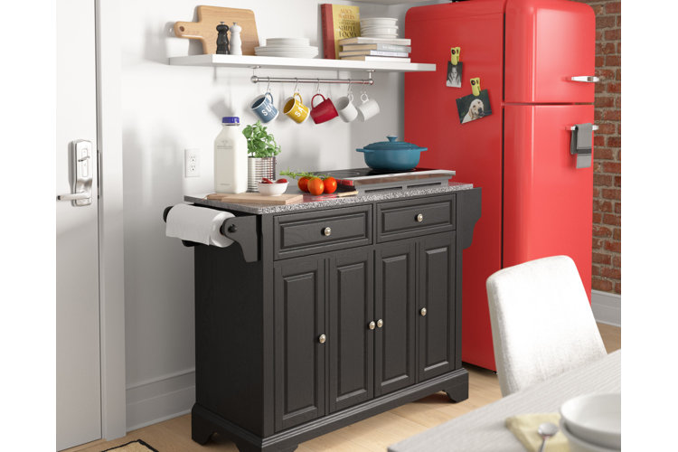 kitchen with a small black island with induction plate, wood cutting board, and blue Dutch oven along with a paper towel holder. Retro-look red fridge next to white floating shelf.