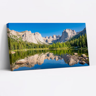 Tableau sur toile représentant des sommets montagneux et des pins se reflétant dans un lac