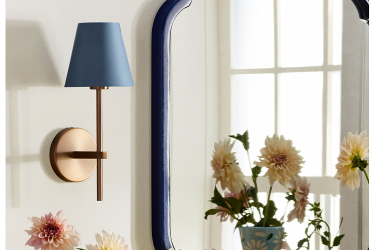 copper Wallchiere wall sconce with a blue lamp shade by a blue mirror and a vase of flowers.