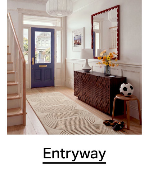Bright, modern entryway featuring a purple front door, a textured dark wood console table, a scalloped-edge wall mirror, and a geometric-patterned runner rug. Entryway.