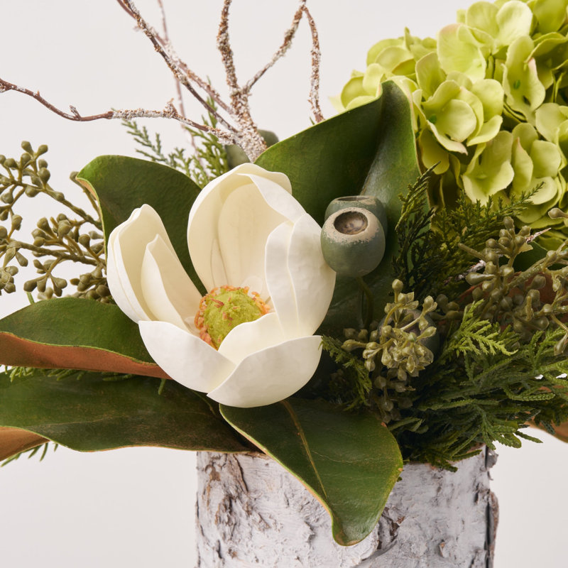 Magnolia des bois - hortensia vert, floraison de magnolia blanc, feuille de toucher véritable et verdure mélangée dans un arrangement de vacances de Noël en cylindre de bouleau blanc