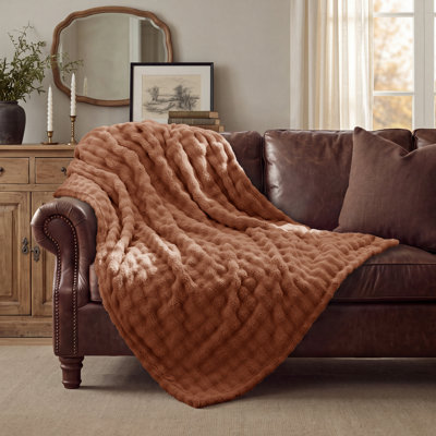Rust-colored throw blanket with a 3D bubble texture draped over a dark brown leather sofa.