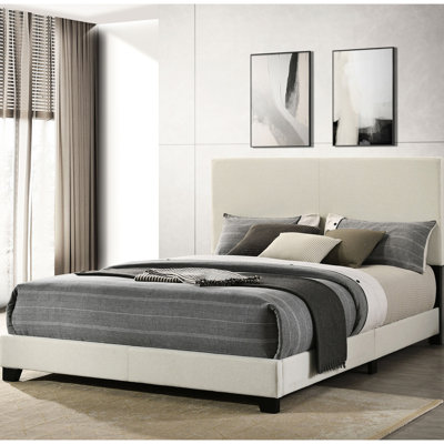 Grand lit tapissier crème avec tête de lit rembourrée, structure en bois et pieds noirs solides, parfait pour les chambres à coucher modernes