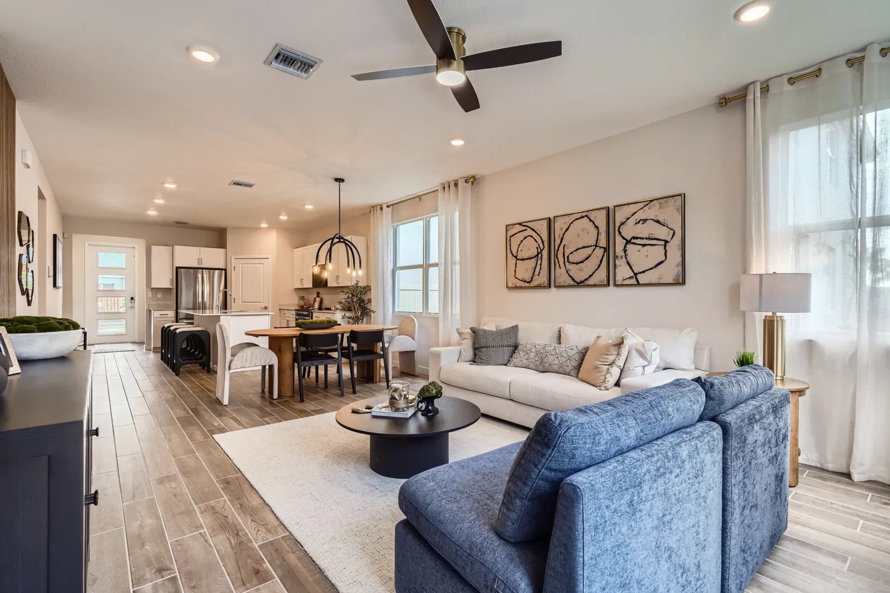 Open-concept living room with white sofa, blue loveseat, and wood-look tile flooring.