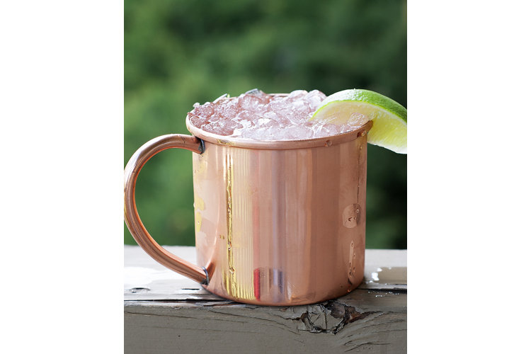 A copper moscow mule mug resting on a porch railing.