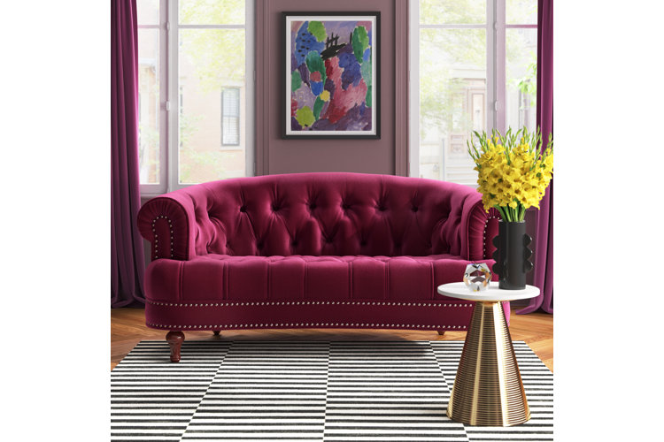 Magenta-colored chesterfield sofa, mauve pink walls, and a striped area rug.